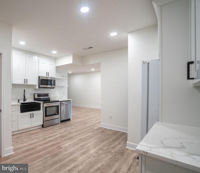 kitchen with stainless steel appliances, a sink, white cabinets, light wood finished floors, and baseboards
