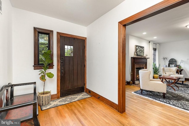 foyer entrance featuring light wood-style flooring, baseboards, a fireplace, and recessed lighting