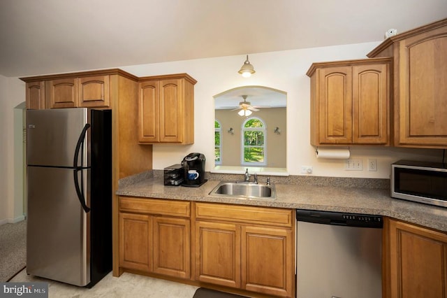kitchen featuring stainless steel appliances, a sink, brown cabinetry, and arched walkways