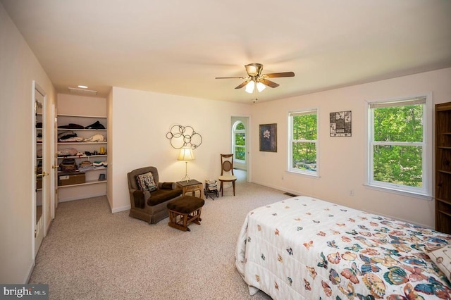 carpeted bedroom with multiple windows, a walk in closet, and ceiling fan