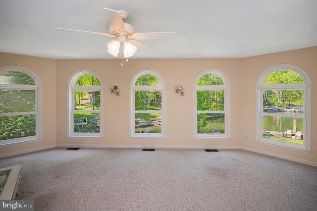 unfurnished room featuring carpet floors, baseboards, ceiling fan, and a water view