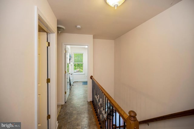 hall featuring baseboards, stone finish flooring, and an upstairs landing