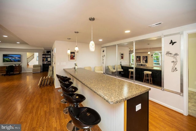 kitchen with wood finished floors, a breakfast bar area, recessed lighting, pendant lighting, and baseboards
