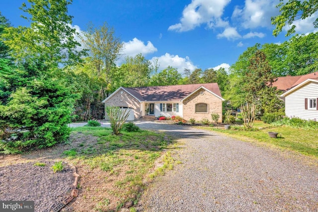 ranch-style house with gravel driveway, an attached garage, and brick siding