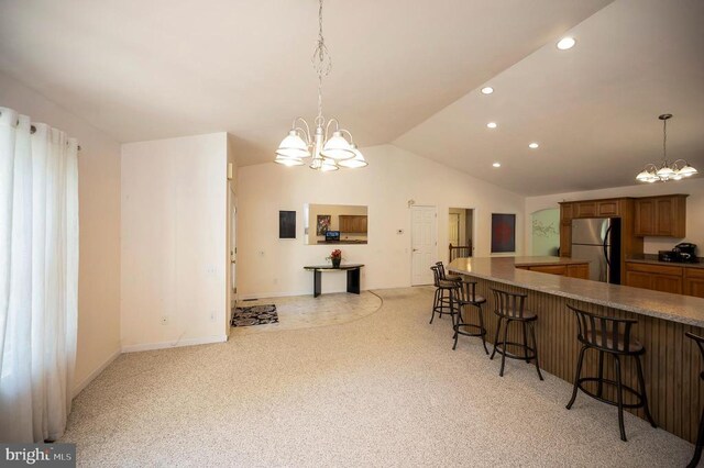 kitchen with freestanding refrigerator, a chandelier, vaulted ceiling, a breakfast bar, and light colored carpet