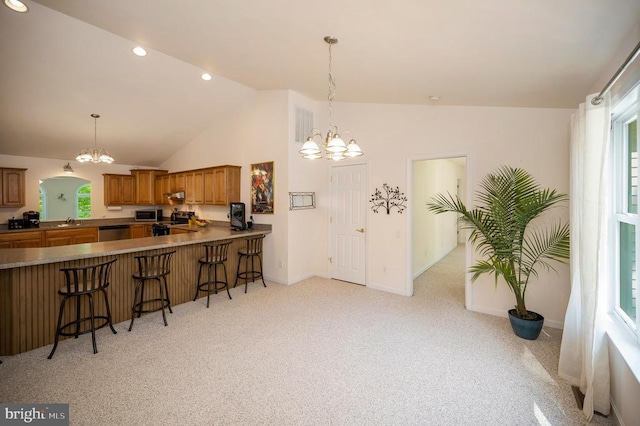 kitchen with stainless steel appliances, a chandelier, a kitchen breakfast bar, light colored carpet, and brown cabinetry