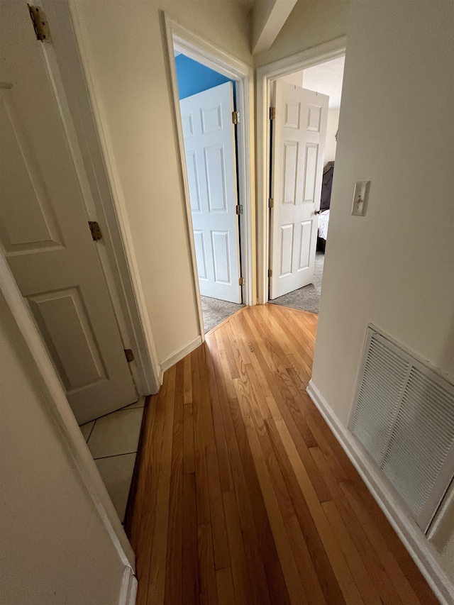 corridor featuring light wood finished floors, visible vents, and baseboards