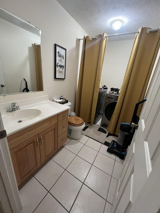bathroom featuring washer / clothes dryer, a textured ceiling, toilet, tile patterned flooring, and vanity