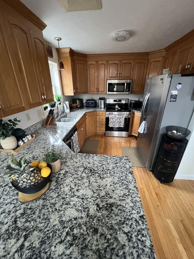 kitchen featuring hanging light fixtures, a sink, brown cabinetry, light wood-type flooring, and appliances with stainless steel finishes