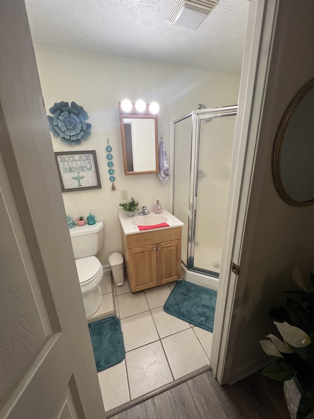 full bathroom featuring a stall shower, a textured ceiling, toilet, visible vents, and vanity