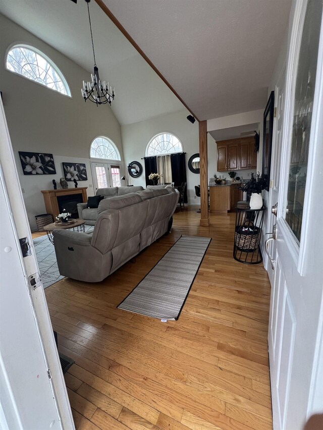 living area featuring a fireplace, an inviting chandelier, light wood-type flooring, and high vaulted ceiling