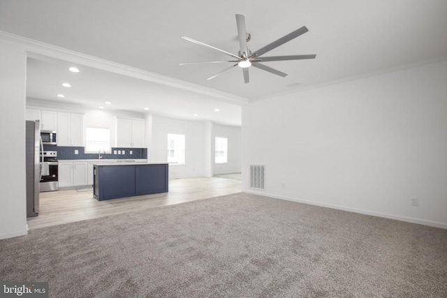 unfurnished living room with ornamental molding, light colored carpet, a ceiling fan, a sink, and recessed lighting