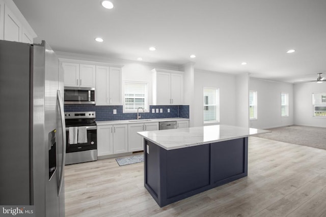 kitchen featuring appliances with stainless steel finishes, open floor plan, white cabinetry, backsplash, and a sink