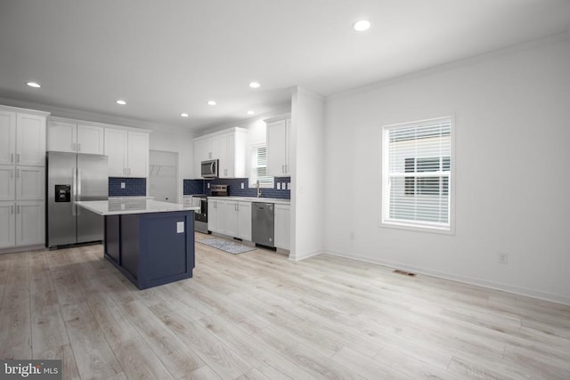 kitchen with stainless steel appliances, tasteful backsplash, a center island, ornamental molding, and light countertops