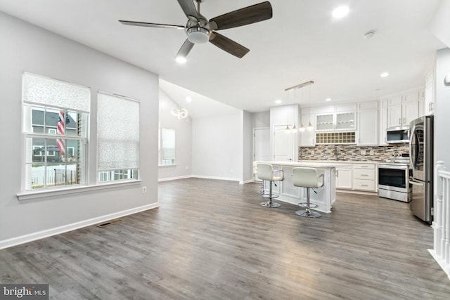 kitchen with stainless steel appliances, backsplash, white cabinets, a breakfast bar, and a kitchen island