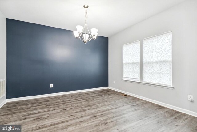 unfurnished room featuring a chandelier, wood finished floors, and baseboards
