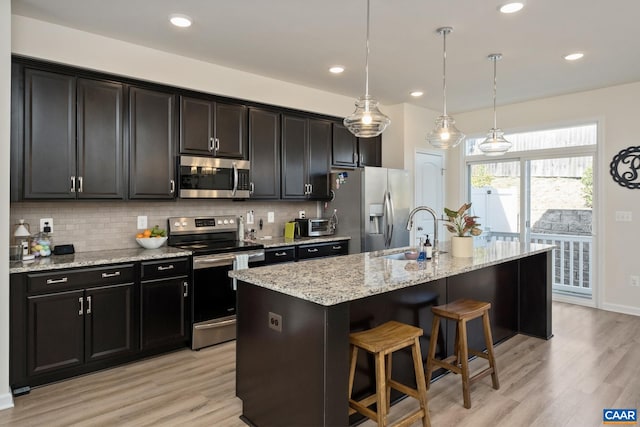 kitchen with light wood-type flooring, a center island with sink, appliances with stainless steel finishes, and a sink