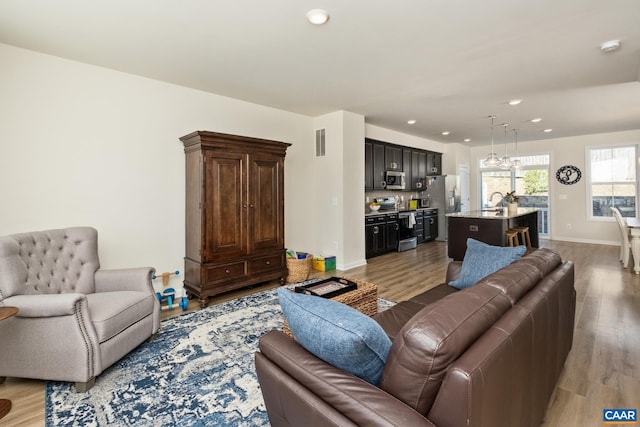 living room featuring light wood finished floors, visible vents, baseboards, and recessed lighting