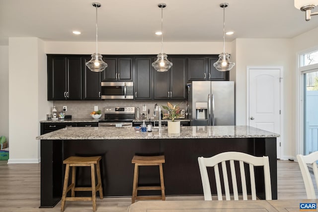 kitchen with tasteful backsplash, dark cabinets, a kitchen breakfast bar, a kitchen island with sink, and appliances with stainless steel finishes