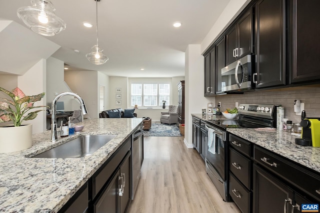 kitchen featuring a sink, light wood-type flooring, backsplash, open floor plan, and appliances with stainless steel finishes