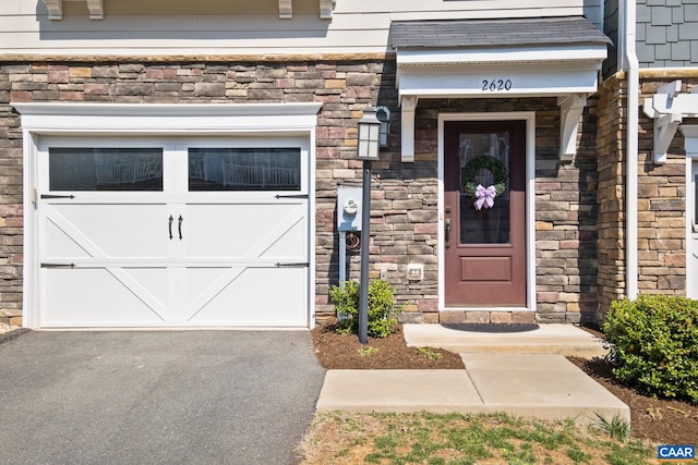 doorway to property featuring a garage, stone siding, and driveway