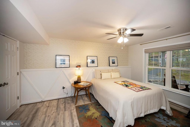 bedroom with wood finished floors, wallpapered walls, and a ceiling fan
