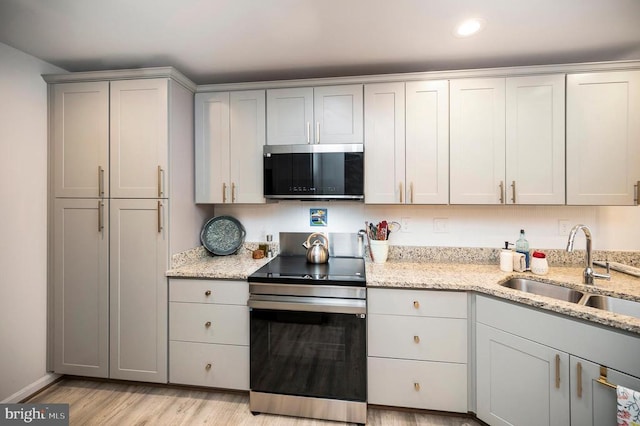kitchen with stainless steel appliances, a sink, light wood-style flooring, light stone countertops, and recessed lighting