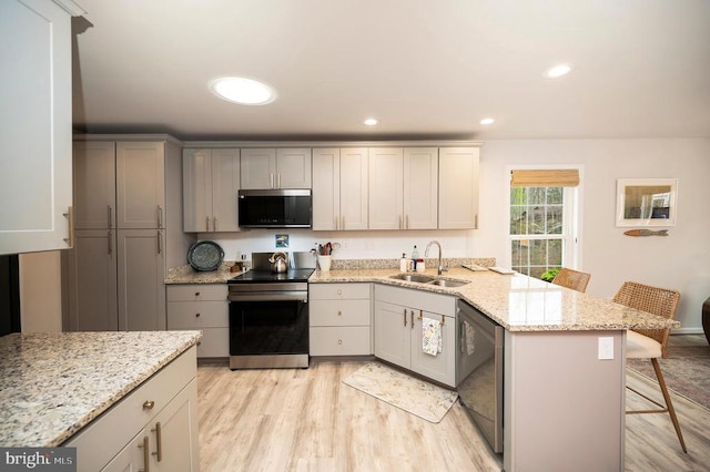 kitchen with appliances with stainless steel finishes, a sink, light wood-type flooring, a peninsula, and a breakfast bar