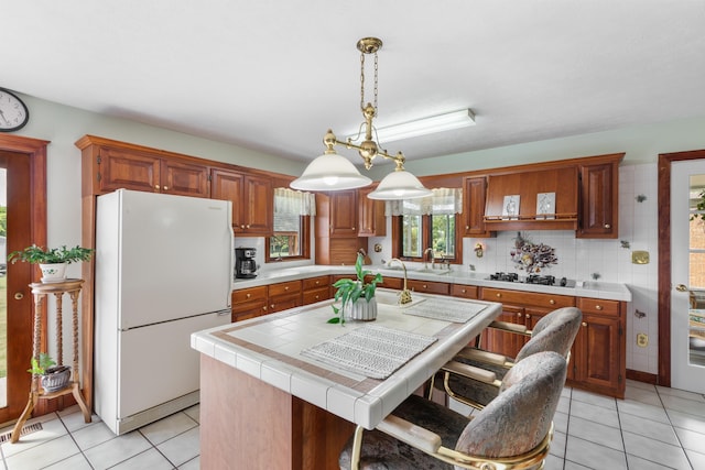 kitchen featuring freestanding refrigerator, light tile patterned flooring, tile counters, a kitchen island with sink, and black gas stovetop