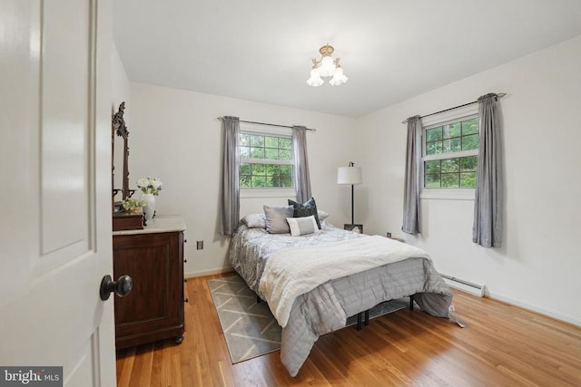  - bedroom with light wood-type flooring, a chandelier, baseboard heating, and baseboards