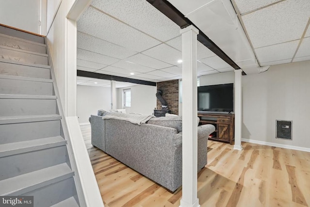  - living area with wood finished floors, stairway, a paneled ceiling, baseboards, and a wood stove