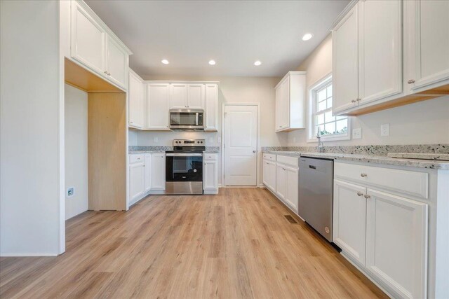 kitchen featuring white cabinets, stainless steel appliances, light wood-style flooring, and light stone countertops