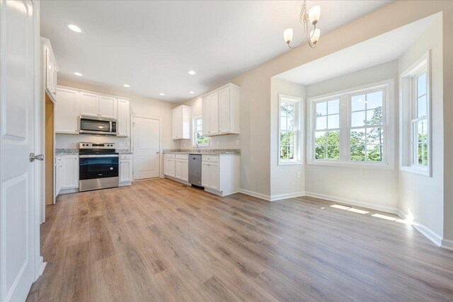 kitchen with stainless steel appliances, light wood-style flooring, baseboards, a chandelier, and white cabinets