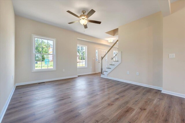 unfurnished living room featuring stairway, ceiling fan, wood finished floors, and baseboards