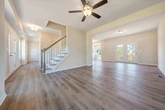 unfurnished living room featuring a ceiling fan, baseboards, visible vents, wood finished floors, and stairway