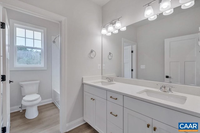 bathroom featuring toilet, double vanity, a sink, and wood finished floors