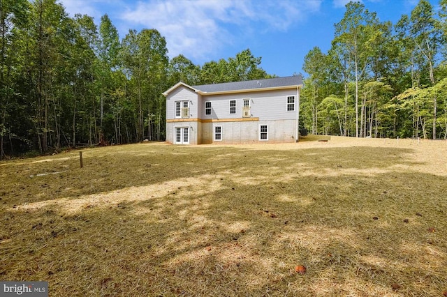 back of house featuring french doors, a lawn, and a wooded view