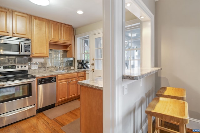 kitchen with light wood finished floors, a sink, stainless steel appliances, light countertops, and tasteful backsplash