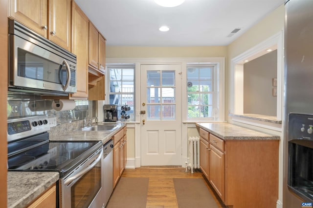 kitchen with a sink, stainless steel appliances, radiator, visible vents, and light wood-style flooring