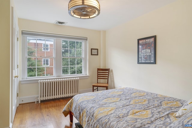 bedroom with visible vents, wood finished floors, baseboards, and radiator heating unit