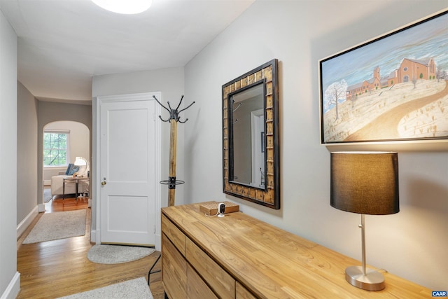 corridor with arched walkways, baseboards, and wood finished floors