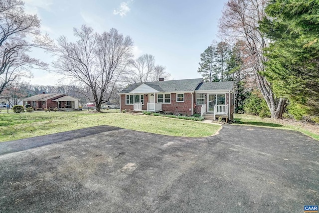 single story home with asphalt driveway, brick siding, a chimney, and a front yard