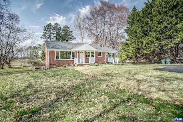 ranch-style home with brick siding, covered porch, a front lawn, and a chimney