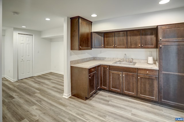 kitchen featuring a sink, light countertops, light wood-style floors, dark brown cabinetry, and recessed lighting