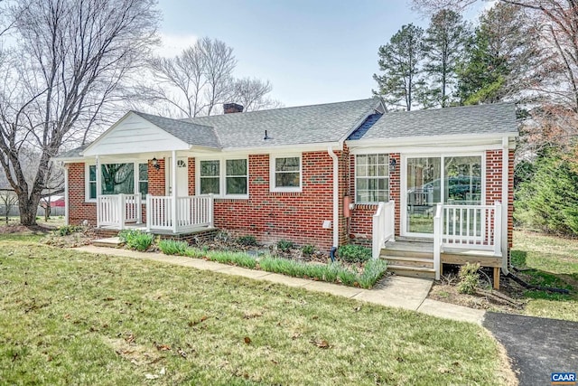 ranch-style home featuring brick siding, a front yard, roof with shingles, and a chimney
