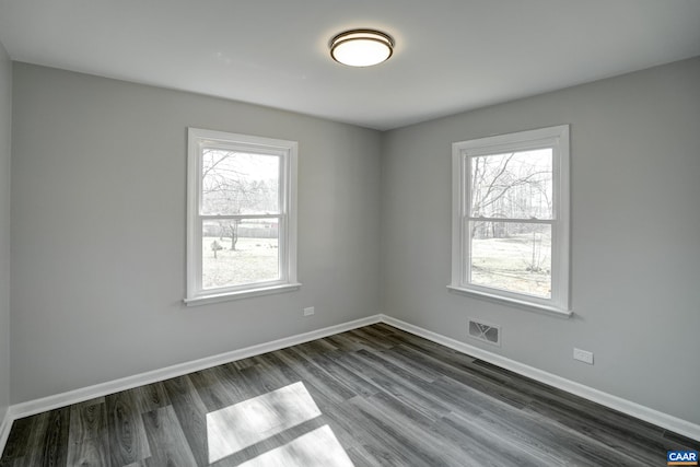 spare room featuring baseboards, visible vents, and dark wood finished floors