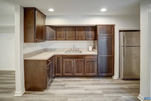kitchen with freestanding refrigerator, a sink, dark brown cabinetry, light wood-style flooring, and baseboards