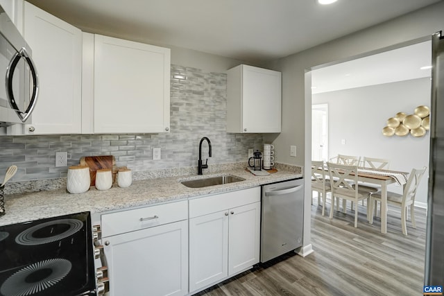 kitchen featuring stainless steel appliances, a sink, light wood-style floors, tasteful backsplash, and white cabinets