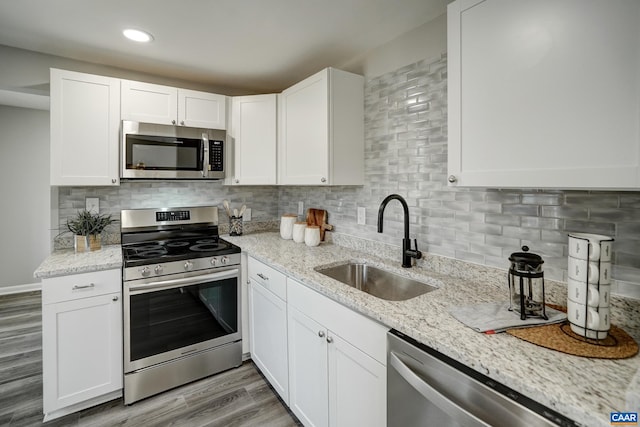 kitchen with stainless steel appliances, a sink, white cabinetry, light stone countertops, and decorative backsplash