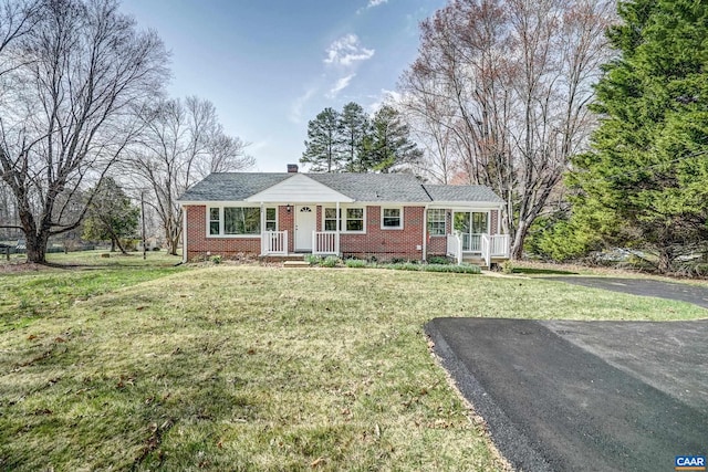 single story home featuring brick siding, a front lawn, a porch, and a chimney